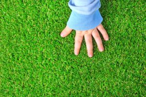 child's hand touching artificial grass